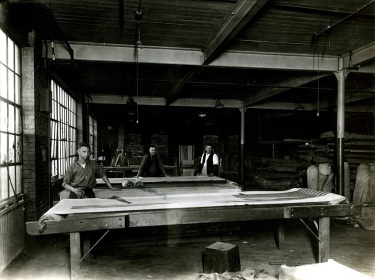 PREPARING RUBBER STOCK - Here the rubber, as it comes from the Calender, is cut to proper length, gauged and inspected, then placed in books or pockets ready for the Tire builders.